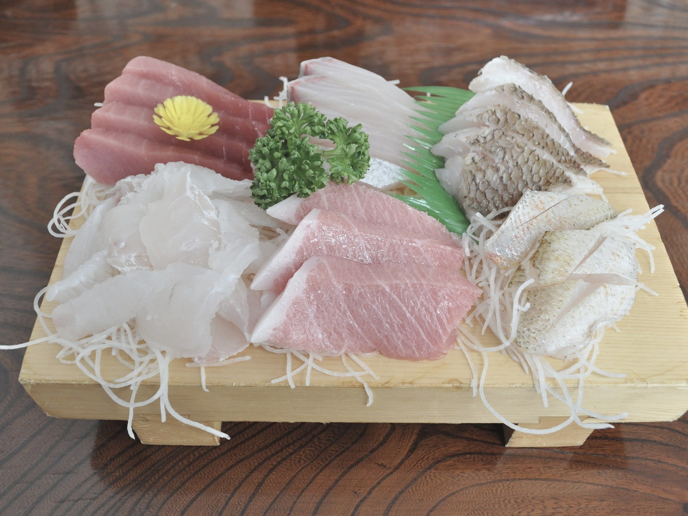Cortes de sashimi de atún y pescado blanco sobre una tabla geta de madera clara